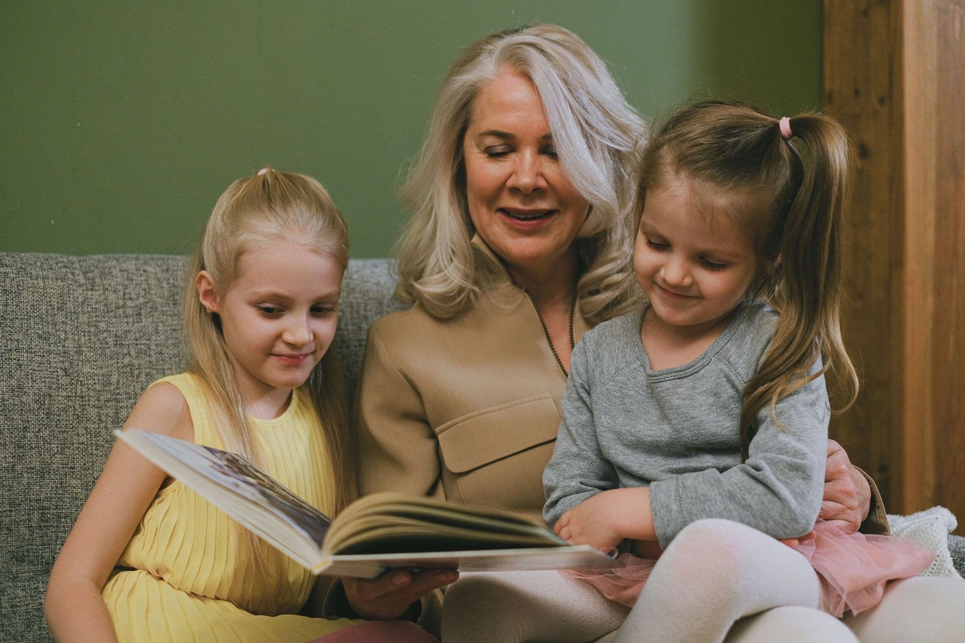 Une grand-mère lit un livre à ses deux petites-filles sur le canapé.